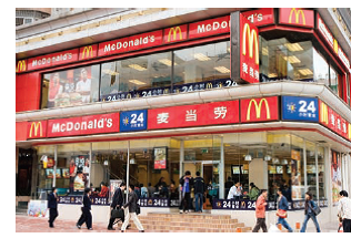 Case Study: Scale Economies and Diseconomies at McDonald's How does having a menu that is uniform around the country provide McDonald's with economies of scale? How is menu planning made more complex by expanding into other countries? Reference Case Study: World of Business Scale Economies and Diseconomies at McDonald's McDonald's experiences economies of scale at the plant, or restaurant, level because of its specialization of labor and machines, but it also benefits from economies of scale at the firm level. Experience gained from decades of selling hamburgers can be shared with new managers through centralized training programs. Costly research and efficient production techniques can also be shared across thousands of locations. For example, McDonald's took three years to decide on the exact temperature of the holding cabinets for its hamburger patties. What's more, the cost of advertising and promoting McDonald's through sponsorship of world events such as the Olympics can be spread across 32,000 restaurants in more than 120 countries. Some diseconomies may also arise in such large-scale operations. The fact that the menu must be reasonably uniform across thousands of locations means that if customers in some parts of the country or the world do not like a product, it may not get on the menu, even though it might be popular elsewhere. Another problem with a uniform menu is that the ingredients must be available around the world and cannot be subject to droughts or sharp swings in price. For example, McDonald's considered adding a shrimp salad to the menu but decided not to when advised the move could deplete the nation's shrimp supply. McDonald's has moved aggressively into overseas markets (about 10 percent of the beef sold in Japan goes into McDonald's hamburgers). Planning across so many markets has grown increasingly complex. For example, McDonald's is kosher in Israel, closes five times a day for Muslim prayer in Saudi Arabia, and serves mutton burgers in India, where cows are worshiped, not eaten. Running a worldwide operation also exposes the company to regional risks, such as environmental protests in Brazil, mad-cow disease in Europe, and terrorist bombings of outlets in France, Indonesia, Russia, and Turkey. Change usually comes slowly in some large corporations, but the profit motive has forced McDonald's to reinvent itself. McDonald's has reorganized its U.S. operation into regions, allowing managers in each region more leeway in pricing and promotion. McDonald's has also become more flexible by putting mini-restaurants in airports, gas stations, and Wal-Marts. The company has been opening new stores and closing unprofitable ones. And McDonald's has reduced the time required to develop new products. For example, whereas Chicken McNuggets were seven years in the making, Chicken Wraps took less than a year to develop. This greater flexibility across countries and regions, the increased willingness to close unprofitable restaurants, and the reduction in product development time all reflect McDonald's effort to cope with diseconomies of scale.