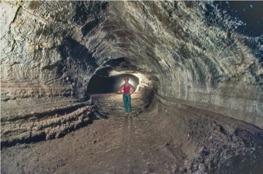   Observe the image of the individual walking through the lava tube. Why is it hollow there and <u>not</u> solid rock? A)  The inside of the lava tube was granite, but granite is <u>not</u> resistant to weathering, so has long since eroded away. B)  There are no natural openings within a lava flow. This must be a manmade feature. C)  When lava cools it contracts, leaving large gaps in the middle. D)  Lava on the inside of the tube often remains molten while the outside crystallizes. Sometimes that molten lava flows out, leaving an empty interior. 