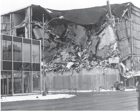 Consider the below photograph.   What does this illustrate about the nature of earthquake destruction? A)  Earthquake destruction takes a long time to occur. In a year's time, the seemingly intact building may look the same as the destroyed building. B)  Earthquake destruction is <u>not</u> widespread. It often destroys only a building or two. C)  Different building codes matter greatly. Buildings that can take earthquake stresses often survive without damage while others build differently face total destruction. D)  Earthquake destruction is very sporadic. Like tornadoes, it may hit one street block hard and completely miss another. 