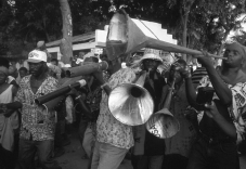 What, in addition to adding to the festive air, do the songs used in a rara performance accomplish for the local culture?   A)  They critique local political conditions. B)  They give the performers a chance to improve their abilities. C)  They allow local subcultures a chance to express themselves openly. D)  They help the musicians become popular on the Internet.