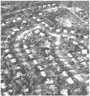 Examine the figure below, which shows a housing development.   In what way(s)  does this use of the land differ from the forest present prior to the construction of the development? A)  The development of roadways creates pathways that encourage the intrusion of nonresident species. B)  The extensive landscaping creates an excess of habitat and promotes overpopulation of selected species. C)  The numerous roofs and paved surfaces prevent rainwater from entering the soil. D)  all of the above