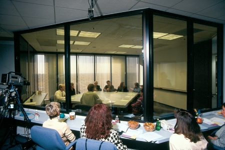   Marketing Research Method Photo C -Consider the Marketing Research Method Photo C above.What type of marketing research method is MOST LIKELY being represented with observers behind a one-way mirror watching a discussion among people about topics of interest to marketers? A)  individual interview B)  questionnaire data C)  social network D)  information panel E)  focus group