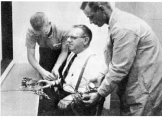 What does this photo show?   A) The man in the middle is having monitors attached to measure his heart rate, pulse rate, and blood pressure as part of Sherif's Robbers Cave experiment. B) A participant is being fitted with a bulky, concealed microphone in Latané and Darley's studies of helping behavior. C) The man in the middle is being strapped to the ―electric chair‖ as part of Milgram's obedience studies D) This is a movie scene involving an interrogation using electric shock that was watched by participants in Zimbardo's famous Stanford Prison Experiment.