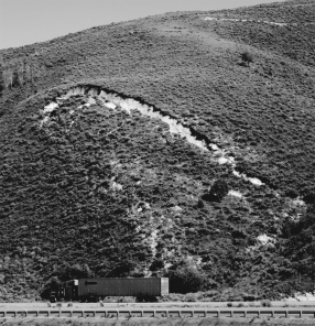 In the figure below,what would be the most effective way to stabilize the slope,assuming that the slope is in a dry,desert environment?   A) regrade the slope B) move the road C) add more vegetation D) install riprap