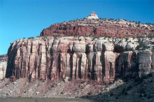 What are some components of the landscape shown in this photograph?   A) a natural stain on the outside of the rocks B) fractures and layers C) loose rocks covering a slope-forming unit D) rounding of the upper parts of the cliff E) All of these.