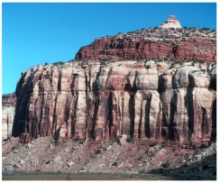 What are some components of the landscape shown in this photograph?   A) a natural stain on the outside of the rocks B) fractures and layers C) loose rocks covering a slope-forming unit D) rounding of the upper parts of the cliff E) all of these