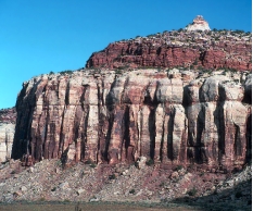What are some components of the landscape shown in this photograph?   A)  a natural stain on the outside of the rocks B)  fractures and layers C)  loose rocks covering a slope-forming unit D)  rounding of the upper parts of the cliff E)  all of these