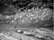 The oldest unit or feature in this photograph is:   A)  the rock at the top that contains angular fragments B)  the gray layer in the middle of the photograph C)  the tilted rocks at the bottom D)  there is no way to tell