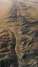 What features in the image help you identify the location of the fault?   A)  Stream channel runs parallel with faults B)  Linear ridges and valley C)  Scarp D)  All of these