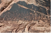 How does this desert feature form?   A)  the Sun bakes and darkens the rock B)  wind coats the surface with material that becomes iron and manganese oxides C)  blowing sand removes material from the rock face D)  vandals painted dark paint over the artwork