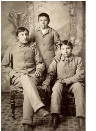 The portraits of Indian students in  The Assimilation of Sioux Students at Carlisle Indian School  illustrate what goal of Indian schools?     A)  To help Indian students maintain ties to their heritage B)  To erase signs of students' Indian heritage C)  To educate Indian students as well as their white counterparts D)  To encourage patriotism to the United States among Indian students