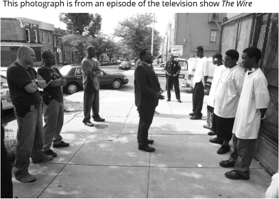 Which of the following represents a sociological interpretation of this photograph?   A) Criminal justice officers,as well as criminal suspects,are mostly male. B) The Wire depicts common beliefs and attitudes,such as the notion that crime and criminal justice are mostly male domains. C) Popular media does not correspond to reality;this is simply a fictional depiction of an imagined world. D) Popular media predicts reality;thus,we can expect more street confrontations such as this one.