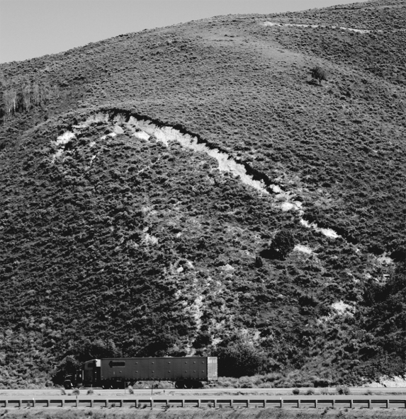 In the figure below,what would be the most effective way to stabilize the slope,assuming that the slope is in a dry,desert environment?   A)  regrading the slope B)  moving the road C)  adding more vegetation D)  installing riprap