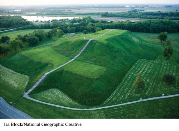 What evidence in this photograph suggests that Monks Mound served as the political and religious center of the Mississippian community at Cahokia?   A)  It appears that no other mounds were built nearby. B)  It was located near the confluence of the Missouri and Mississippi Rivers. C)  It has a multitiered design. D)  It is enormous in size with a large, flat top tier.
