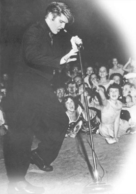 <strong> What was one major reason as shown in this photograph that rock-and-roll singer Elvis Presley contributed to the growing generation gap between parents and their teenaged children during the 1950s?</strong> A) His clean-cut image was acceptable to parents but rejected by their adolescent children. B) His suggestive moves enraged parents while gaining adoring teenaged fans. C) Parents enjoyed his catchy lyrics and music while young people thought they sounded too black. D) Parents saw his success as a triumph for consumer tastes while their children saw it as the downfall of American civilization.