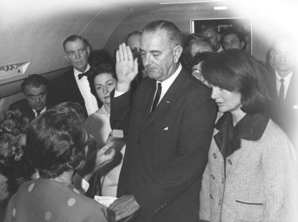   -Why did Lyndon B. Johnson insist on taking the oath of office with Jackie Kennedy at his side after John F. Kennedy's assassination in Dallas as shown in this photograph taken by Cecil Stoughton? A)  to demonstrate to the public that she supported his presidency B)  to put a stop to widespread rumors that he had no right to the presidency C)  to show that the supposed friction between him and President Kennedy was a myth D)  to quell suspicions that he had had a hand in the assassination of President Kennedy