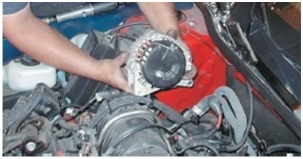 What component is the technician holding?   A) Water pump B) Alternator C) Compressor D) Wiper motor