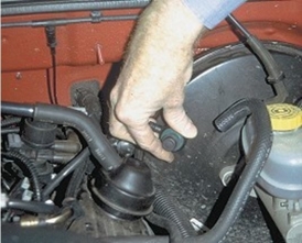 What component is the technician holding in this photograph?   A) Fluid plug B) Check valve C) Vacuum sensor D) Vacuum elbow
