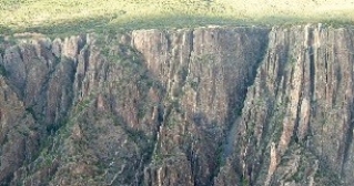 136) What type of rock likely composes the landscape shown in this photograph from the Investigation?   A) sedimentary rocks B) granite C) metamorphic rocks D) volcanic rocks, probably basalt